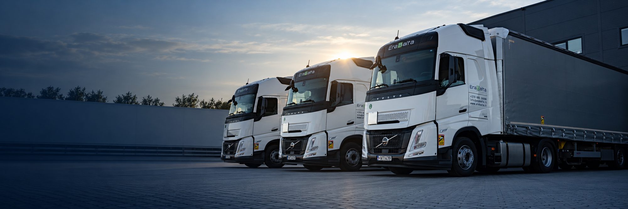 Completed transports: three Erabalta trucks at a logistics terminal at sunset